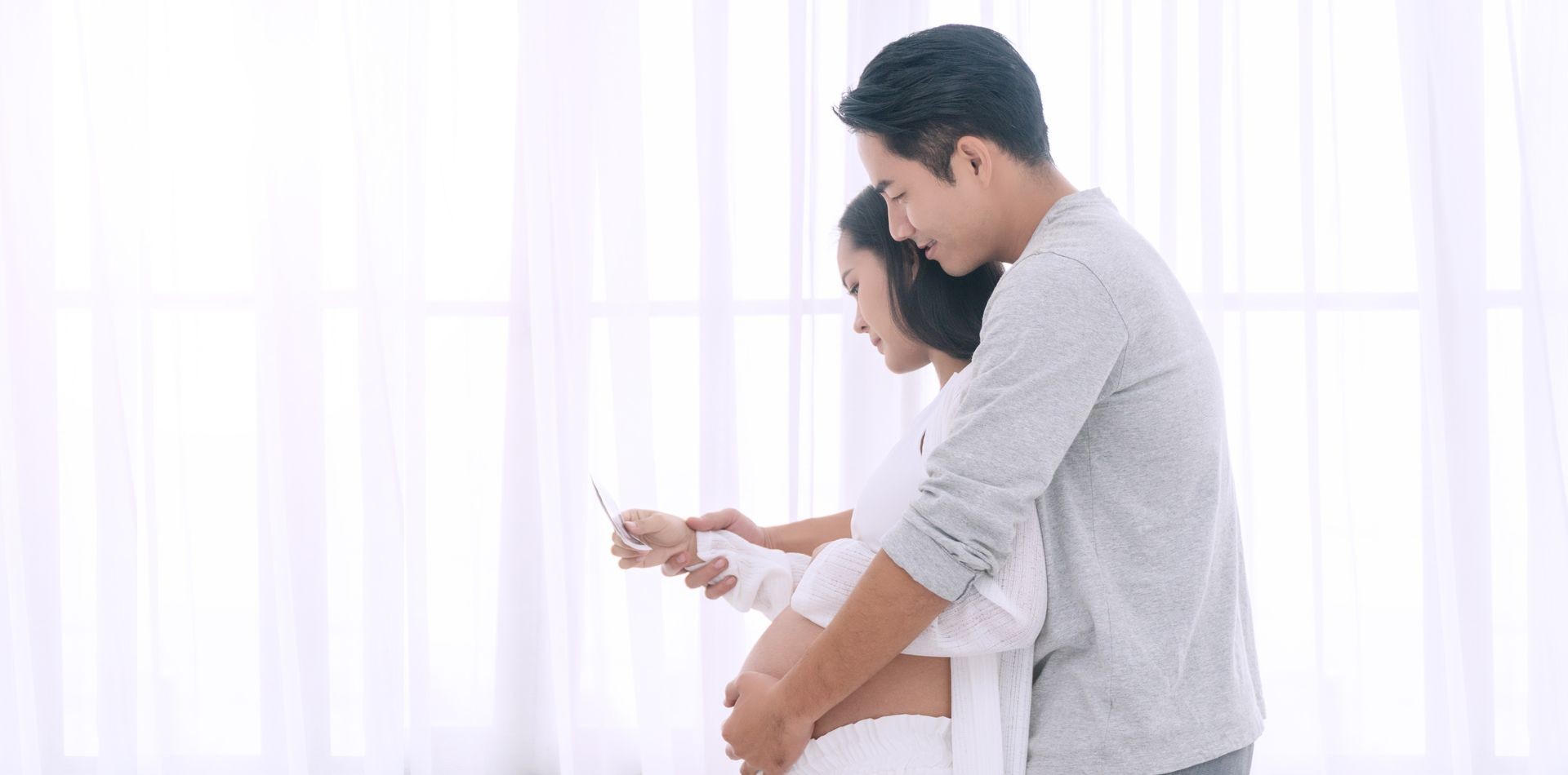 Husband embracing his wife's belly with love. Happy couple of young man hugs his pregnant beautiful wife , smiling and looking at the ultrasound pregnancy photo at home with copy space.