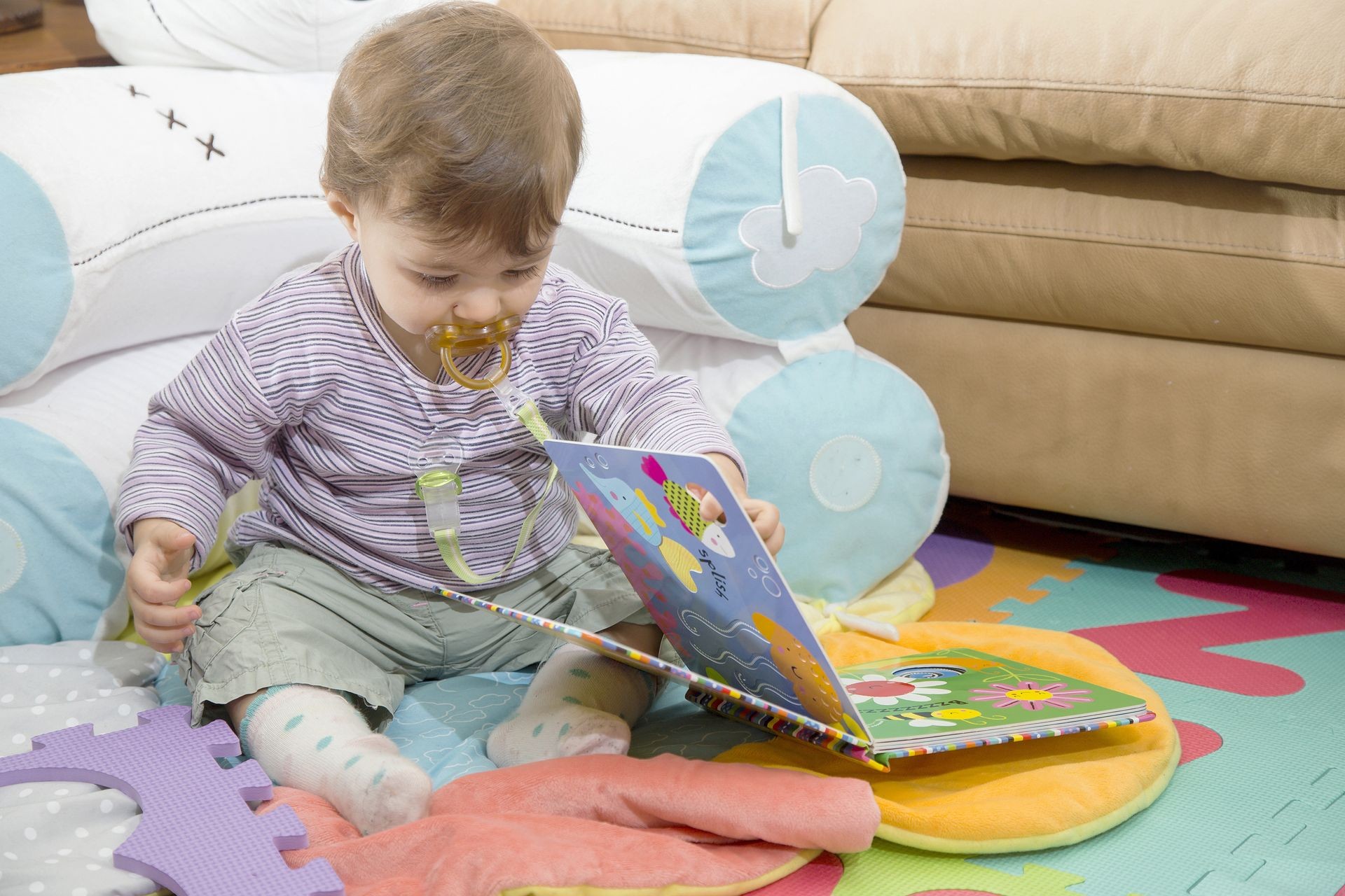 Lovely one year old baby with colorful book sitting on floor at home