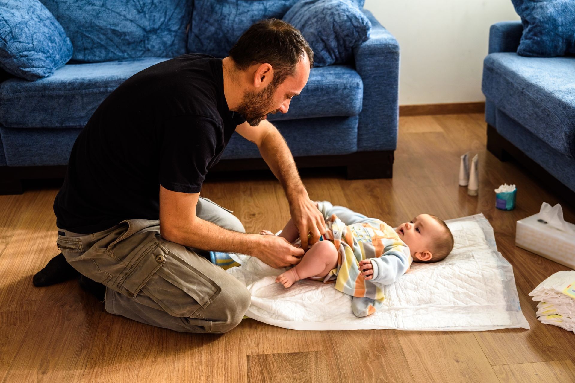 Father changing his daughter's dirty diaper on the living room floor.